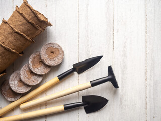 Gardening at home. Tools, peat pots and pressed ground for seedlings. Flatlay on white wooden background.