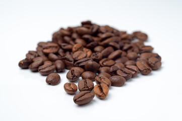 Dark, roasted coffee beans pile on a white surface.
