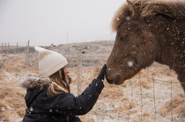A girl touching icelandic horse, winter time, snowflakes