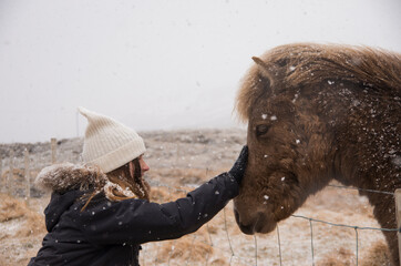 A girl touching icelandic horse, winter time, snowflakes