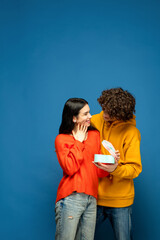 Fototapeta premium Sweet candies. Beautiful couple in love on blue studio background. Saint Valentine's Day, love, relationship and human emotions concept. Copyspace. Young man and woman look happy together. Flyer