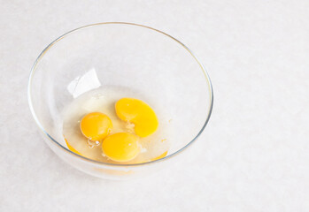 Four yellow yolks with egg protein in a deep plate  before cooking on a white isolated background.