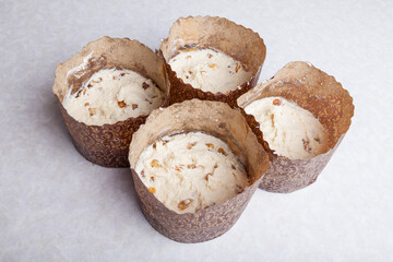 Four tins for baking muffins at home made of brown cooking paper filled with raw raisin dough on a white table. Home hobby baking Easter cakes.