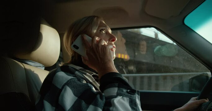 Mature blonde driving car and talking on phone, lost in city, risks on road