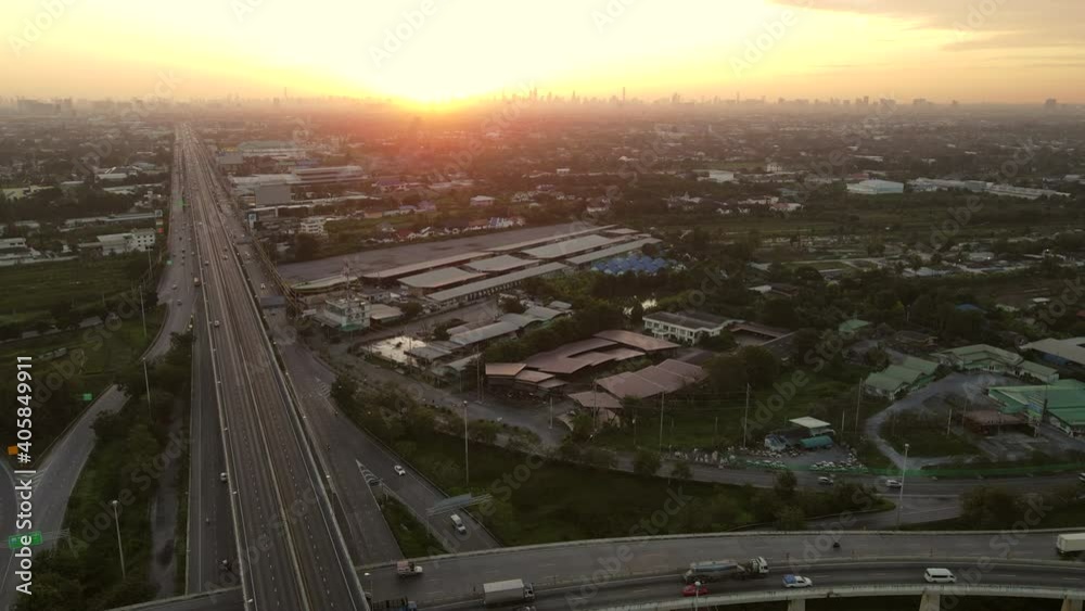 Wall mural 4k. aerial view of urban road leading to the city during sunrise with busy urban traffic speeding on