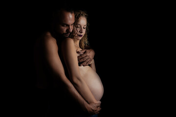 Naklejka premium naked pregnant woman and her husband posing at the camera on a black background