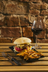 Cheeseburger with fries and a glass of wine on a brick wall background