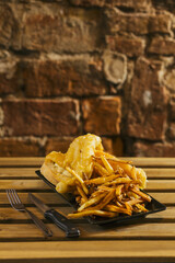 A fish and chips plate with fries on a brick wall background