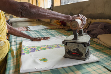 Undidentified senior woman ironing clothes with an old coal heated iron in India