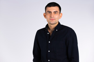 An elegant and stylish man in a black shirt on a white background in the studio with empty side space.