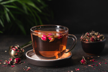 Fresh tea from rose petals in glass cup. Pink hot drink on dark brown background