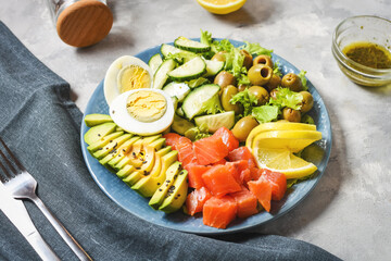 Ketogenic, paleo diet lunch bowl with salted salmon fish, lemon, avocado, olives, boiled egg, cucumber, green lettuce salad, healthy food