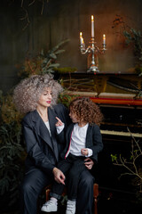 Mother with little daughter wearing stylish clothes on the background piano and candlestick.