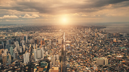 Sun over city roofs of skyscrapers buildings aerial. Urban traffic road at streets of downtown. Philipines capital cityscape at summer sunlight. Filipino town cinematic soft light drone shot
