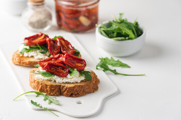 Bruschetta with sun dried tomatoes and arugula. Delicious breakfast or wine snack. White background, close-up, top view