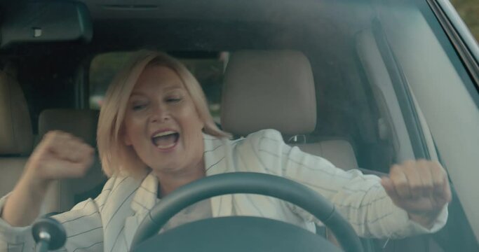 Extremely happy aged businesswoman turning on car radio and moving to music