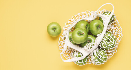 Green apples in mesh bag. Pastel yellow background