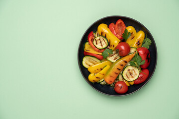 Variety of grilled vegetables in bowl on yellow background. Zucchini, bell peppers, hot peppers, tomatoes and green parsley