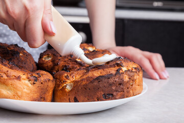 Close-up of decorating freshly baked cupcakes by squeezing white icing from a tube with a female hand - making Easter cakes at home using ready-made products according to the recipe.