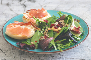 Breakfast of fresh salad and two halves of a bagel with cheese and prosciutto.