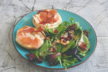 Breakfast of fresh salad and two halves of a bagel with cheese and prosciutto.