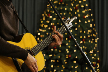Young man playing guitar.Festive atmosphere around - bright bokeh on the background.Close up...
