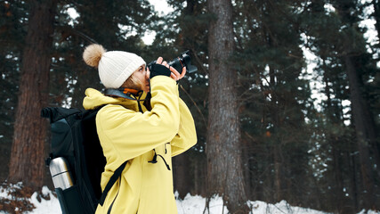 A girl with a backpack and a yellow anorak photographs the landscape on a professional camera