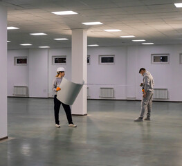 Workers measure the distance with a tape measure. A man and a woman in work clothes measure the room with a tape measure, referring to the drawings.