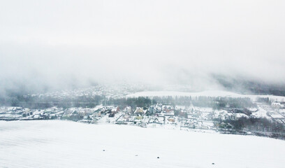 Top view of snow-covered houses in suburb near fields in winter