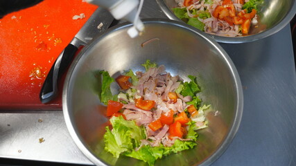 Male arms of cook in gloves pouring mayonnaise onto fresh ingredients in iron bowl at kitchen. Chef preparing tasty caesar salad at cuisine. Concept of cooking food. Top view Slow motion