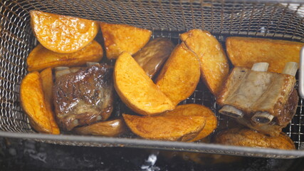 Male cook shaking a lattice with slices of potatoes rustic and meat in hot boiling oil. Chef lowering a grid with pieces of potatoes village into deep fryer. Concept of preparing food. Top view