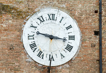 Close-up of an antique big marble clock with Roman numerals on the brick wall of an old building,...