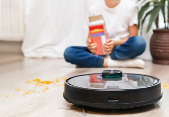 Obraz na płótnie Canvas Robotic vacuum cleaner ready to easily remove the flakes, which were scattered by child during eating. Focus is on the robotic vacuum cleaner with blurred background. Smart home, housework concept. 