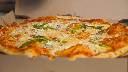 Male hand of chef in glove finishing tasty vegetarian pizza with a sprinkles grated parmesan at cuisine restaurant. Delicious baked dish in a carton box at kitchen pizzeria. Close up Slow motion