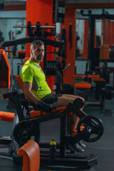 Fototapeta na wymiar Side view of a middle-aged man with a yellow fluorescent shirt exercising on the machine for legs.