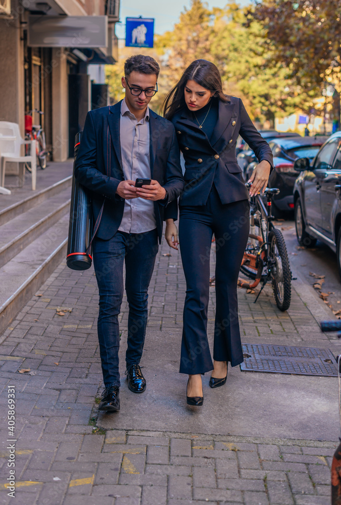 Wall mural Business man and woman holding mobile phone and talking standing on the streets