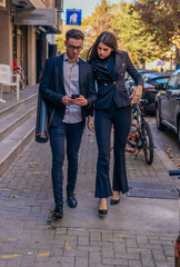 Obraz premium Business man and woman holding mobile phone and talking standing on the streets