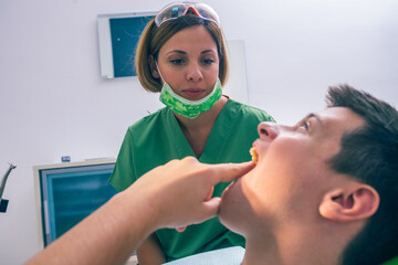 Closeup image of a teenage boy patient showing his toothache to his female dentist in the dental office.