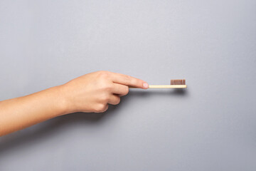 Hand holding toothbrush. Bamboo eco brush. Dental sustainable concept. Layout. Morning home routine. Grey background. Medicine cosmetics. Mouth hygiene treatment. Personal cleaning. Copyspace