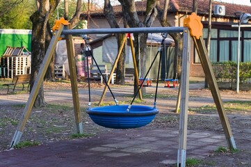 Fototapeta premium A wooden swing with a circular blue rubber seat in a public park (Pesaro, Italy, Europe)