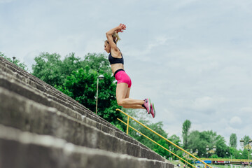 Fit healthy athlete, beautiful woman in tight sportswear jumping on stairs, warming up before jogging while looking highly motivated..