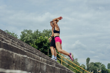 Below view of young male and female athletes jumping upstairs on the outdoor staircase .