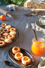Tasty Christmas Linzer cookies filled with orange jam on cooling rack and vintage metal plate. Xmas stollen and fir twigs on table with natural linen tablecloth.