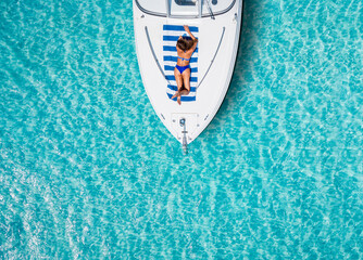 Aerial top down view to a woman in bikini taking a sunbath on a yacht over tropical, turquoise sea