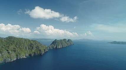 Obraz premium Hilly islands at blue ocean coast aerial view. Nobody nature scenery of Palawan, El Nido Isles, Philippines. Green tropic forest at mount ranges under fluffy clouds on sky. Cinematic drone shot