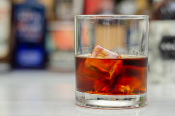 Old fashioned glass with scotch whisky and ice cubes on the bar