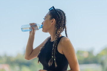 Portrait of a happy female athlete drinking water from a plastic bottle after an outdoor workout