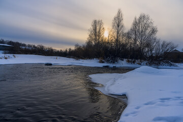 winter landscape with a river. evening on the Neiva River (Russia). white snow lies on the banks. the sun will soon sink below the horizon. sunlight is reflected in the water. yellow clouds
