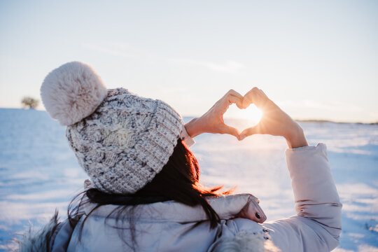 happy young woman hiking in snowy mountain at sunset doing a heart shape with hands. winter season. nature and love