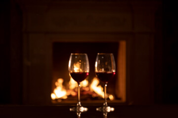 two glasses of red wine - romantic dinner against the background of a burning fireplace 